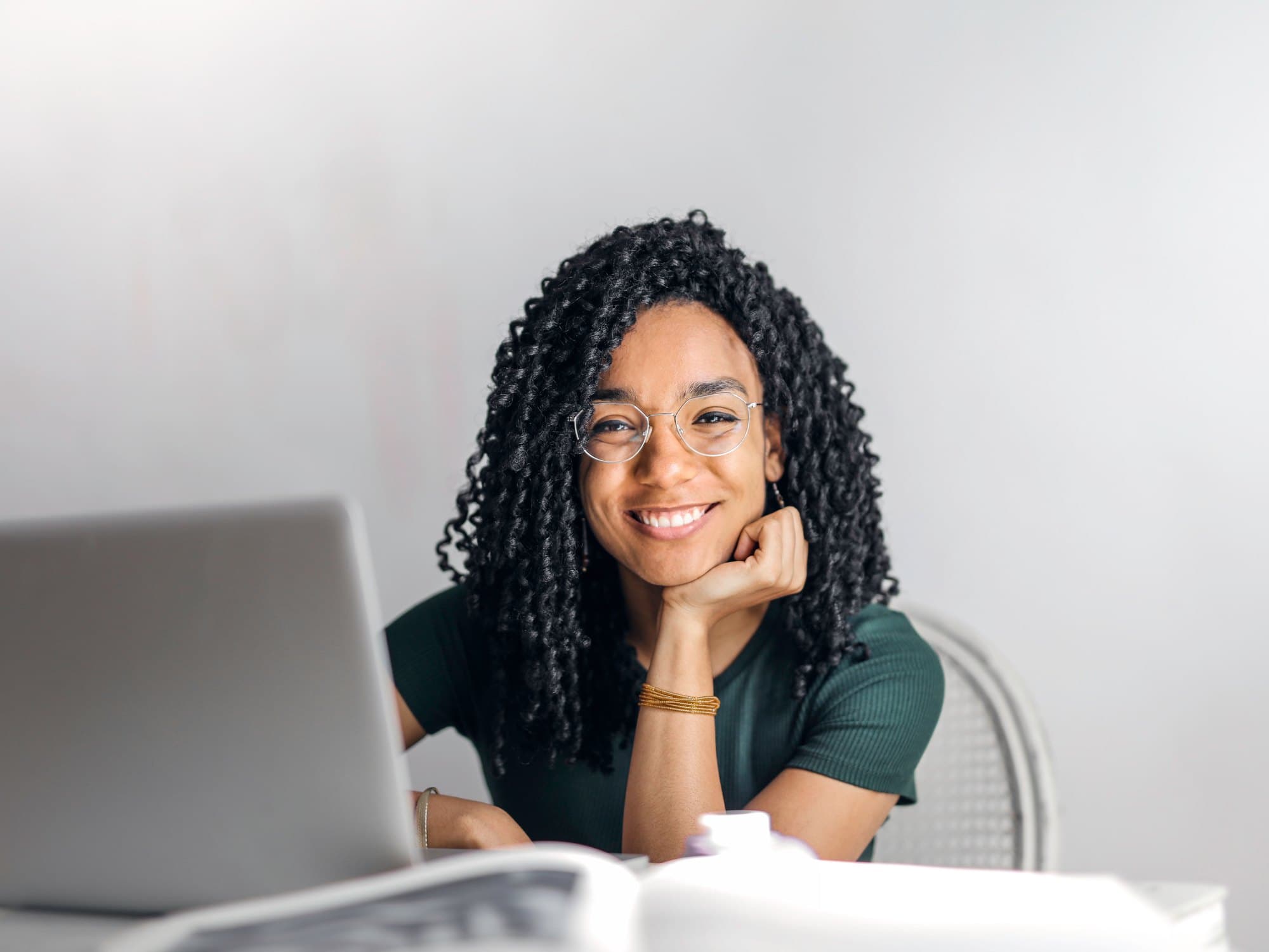 A woman in a teal-green shirt smiling at a desk beside a laptop
