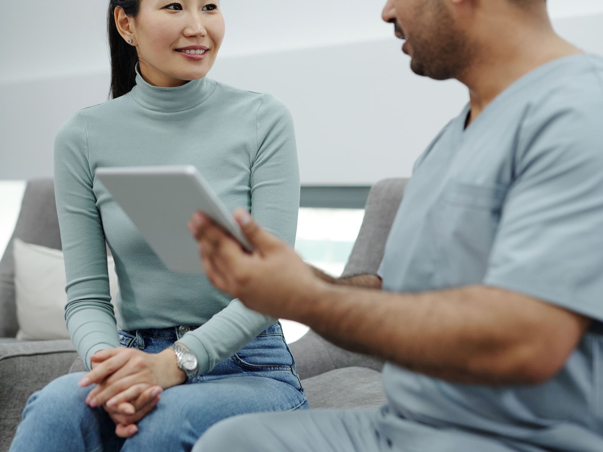 Two adults reviewing information on a tablet, one wearing clinical scrubs