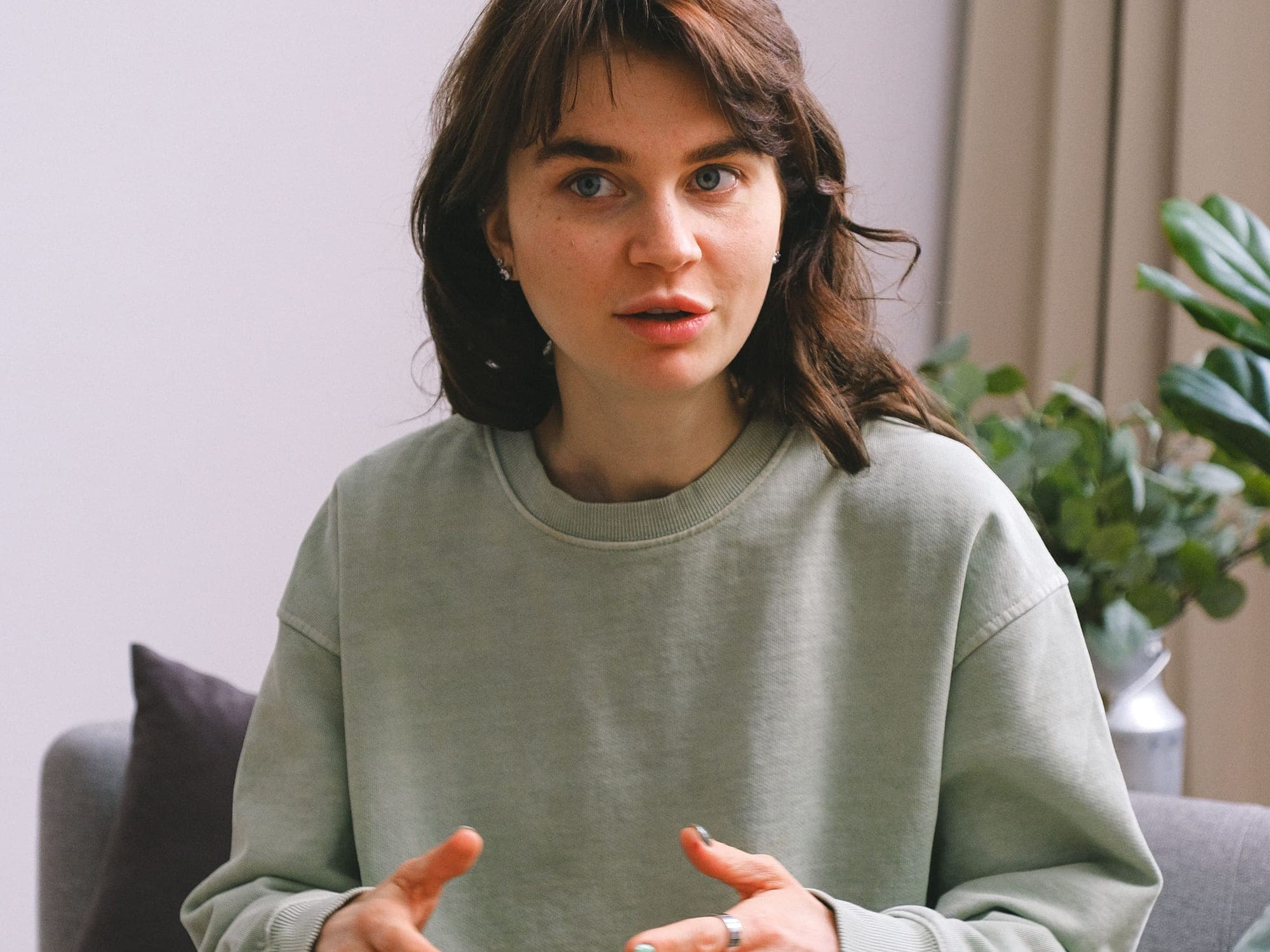 A person in a sage sweatshirt gesturing during a conversation on a sofa