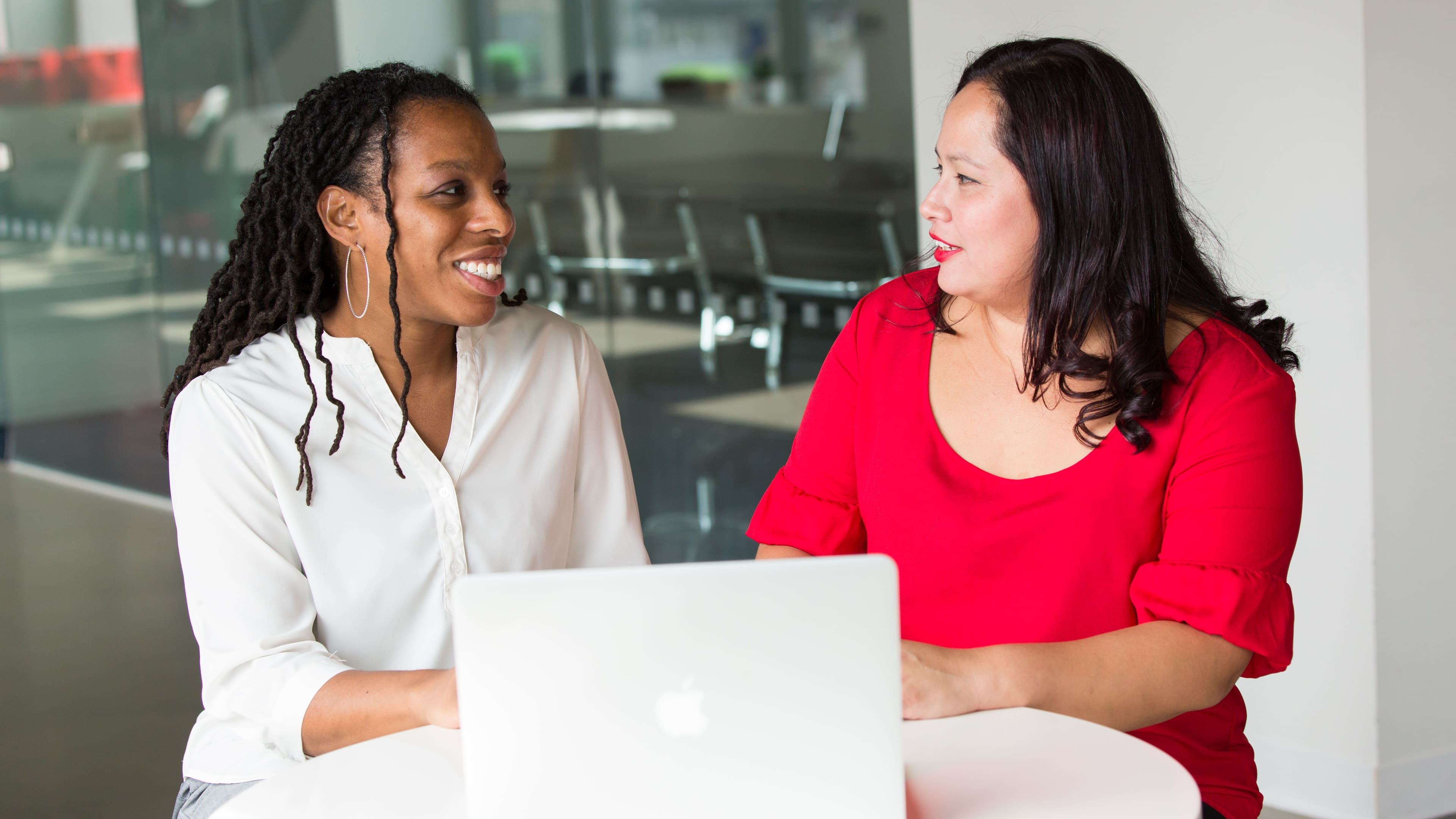 Two people talking across a white table near a window during a consultation